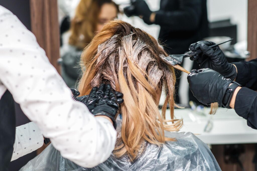 Hairdresser applying hair dye to client's hair with brush in salon