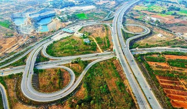 Aerial view of highway cloverleaf interchange with looping ramps surrounded by farmland and greenery"