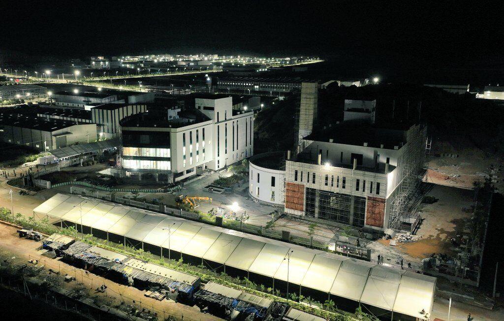 Night aerial view of illuminated industrial complex with modern buildings under construction and covered walkway"